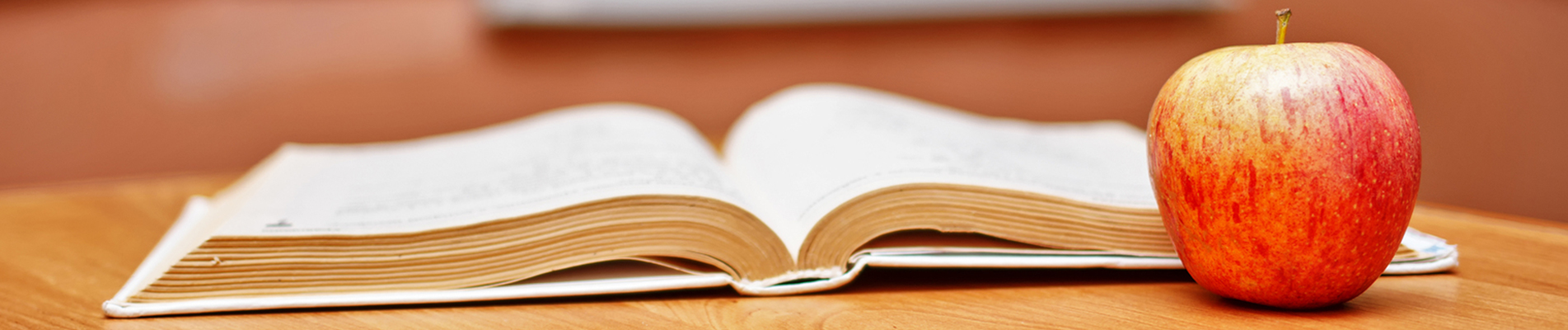 Open book and apple sit on a wood surface