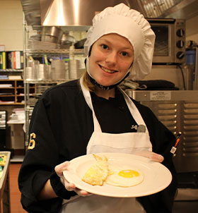 Student in chef's hat holding cooked eggs