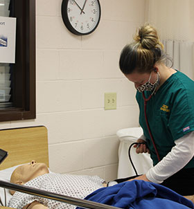 Student practicing taking patient vitals on mannequin